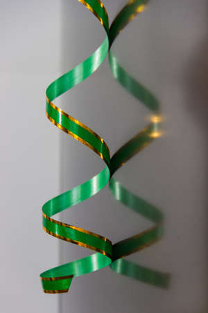 Curly paper streamer of green with golden colors hanging against the matt metal reflective surfaceの写真素材