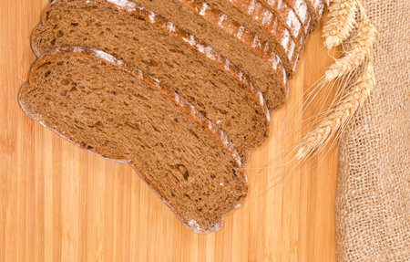 Sliced loaf of hearth brown bread made with wheat and rye flour on a wooden surface, wheat ears on a...