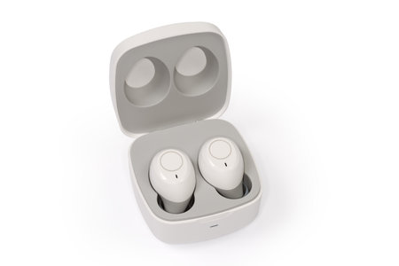 Pair of modern white wireless in-ear earphones in wireless charging case close-up on a white backgroundの写真素材