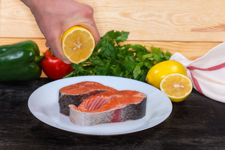 Pieces of fresh uncooked rainbow trout on white dish on a black surface during squeezing lemon juice on them for preparingの写真素材