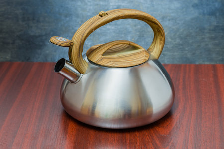 Stainless steel stovetop kettle with open steam whistle on spout on a wooden tableの写真素材