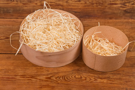 Two small round wooden boxes different size without lids, filled with wooden packing shavings on an...