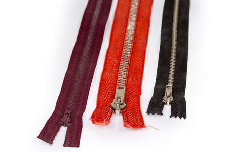 Not sewn zippers different colors with metal teeth and sliders on a white background, fragment close-up in selective focusの写真素材
