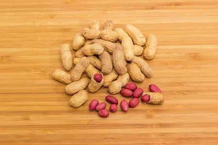 Small pile of dried peanuts in their shells and some peeled peanut kernels on a bamboo wooden...