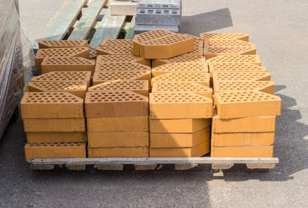 Yellow perforated decorative face bricks with an oblique one angle stacked on wooden pallet on an...