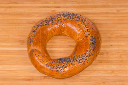 Traditional Eastern European ring-shaped bread roll sprinkled with poppy seeds before being baked lies on a wooden surface, top viewの写真素材