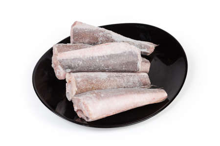Uncooked frozen carcasses of Argentine hake, or hake hubbsi without the heads and tails on a black plate on a white backgroundの写真素材