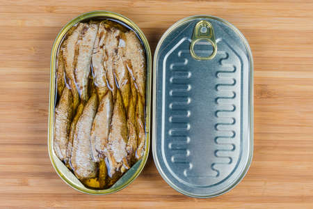 Smoked canned sprats in cooking oil in open tin can and sealed tin can on a wooden surface, top viewの写真素材