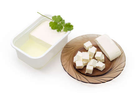 Fresh feta cheese partly diced on glass saucer and the rest cheese soaked in whey in container on a white backgroundの写真素材
