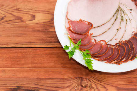 Slices of dry-cured pork tenderloin and baked ham decorated with parsley on dish on an old rustic...