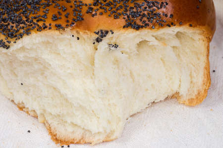 Broken off piece of sweet braided bread sprinkled with poppy seeds on the textile napkin, fragment...