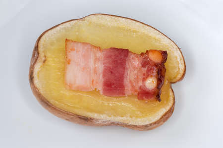 Half of potato in their skin baked together with bacon slice on a white dish close-upの写真素材