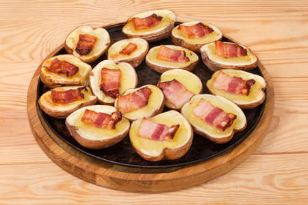 Potato halves in their skins baked with bacon slices on a round baking sheet on a rustic tableの写真素材