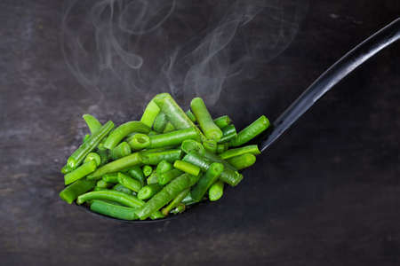 Freshly blanched cut green beans on the black plastic slotted spoon close-up on a dark background