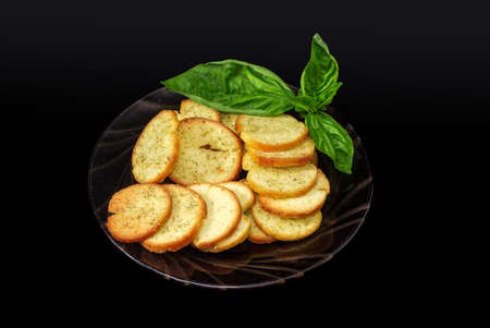 Round spicy rusks with pesto sauce flavor, fresh basil twig on the glass saucer on a black backgroundの写真素材