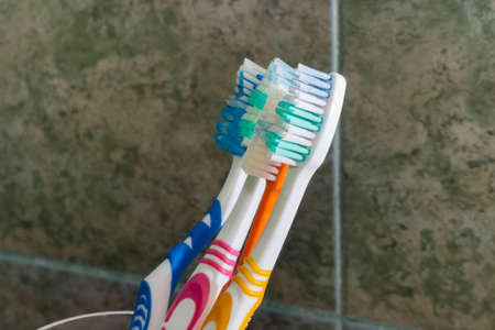 Different toothbrushes on a blurred background of wall in bathroom covered with green tile, close-up...