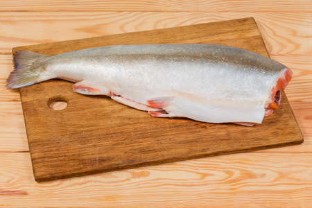 Whole carcass of the fresh gutted uncooked arctic char without head on the wooden cutting board on rustic tableの写真素材