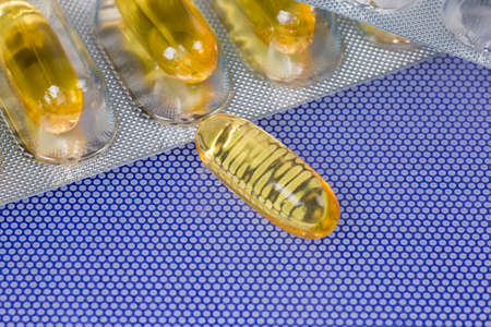 Yellow capsule against blister packing, close-up in selective focus