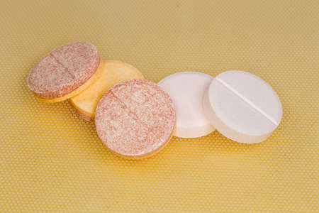 Different effervescent tablets of pharmaceutical product on a yellow surface, close-up in selective...