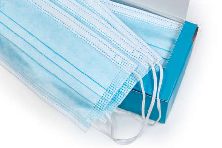 Several light blue disposable medical face masks lie on the open cardboard packaging of the same...