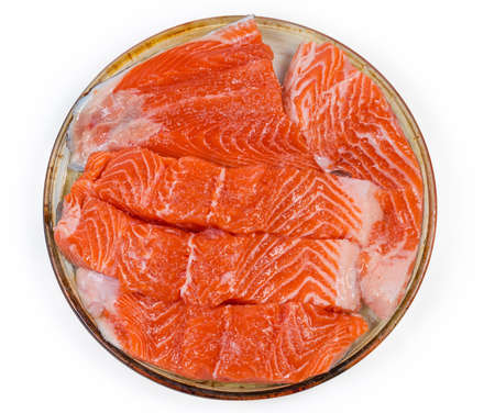 Raw pieces of the rainbow trout fillet prepared for baking on the glass baking dish on a white...