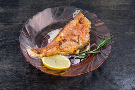 Ocean perch cooked in sour cream sauce on a red glass plate on a dark surface