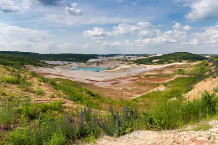 Abandoned china clay pit with small turquoise quarry lake in center against the cloudy sky