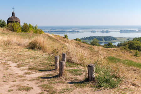High gently sloping bank of wide plain river with small wooden church on a background, in early...