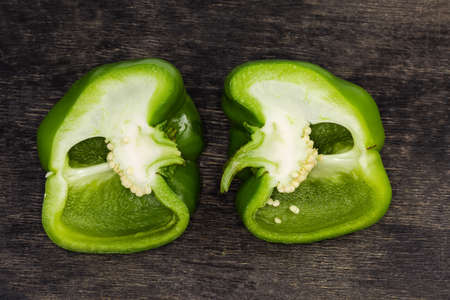 Two halves of fresh green bell pepper cut lengthwise lie on the dark surface, top viewの写真素材