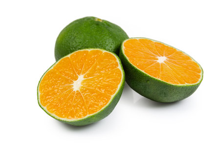 Two halves of the ripe tangerine cut across, variety with a green peel against the same whole tangerine, close-up on a white background in selective focusの写真素材