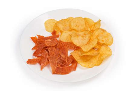 Thin slices of dry chicken snacks and round thin potato chips on a white dish on a white backgroundの写真素材