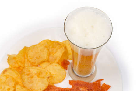 Glass of lager beer on a blurred background of different snacks on a big dish on a white background, top view in selective focusの写真素材
