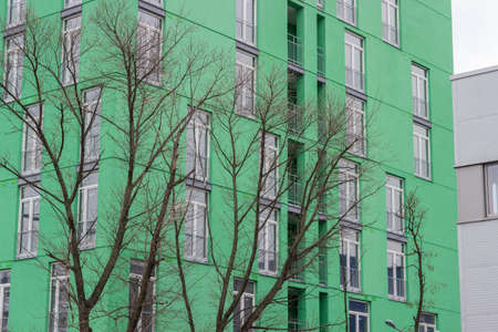 Fragment of the green facade of modern multi story apartment building with trees without leaves on a foregroundの写真素材
