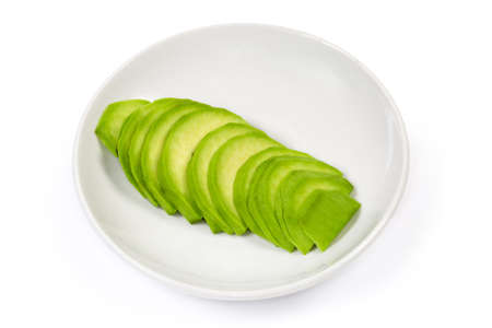 Peeled sliced half of the ripe green avocado fruit on a white saucer on a white backgroundの写真素材
