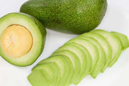 Slices of the ripe green avocado fruit, unpeeled half and whole avocado on a dish, fragment close-up