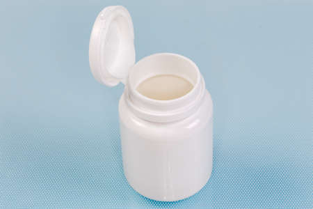 Open small white plastic bottle with medical pills on the blue surface close-up