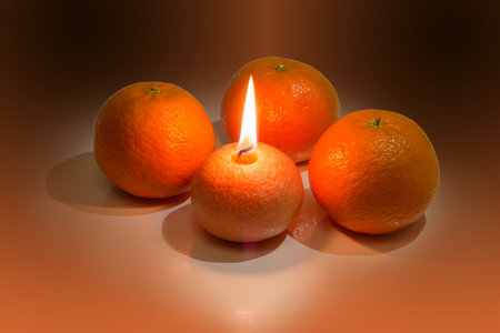 Burning decorative candle in the form of tangerine against the real fresh tangerine fruits on a light surfaceの写真素材