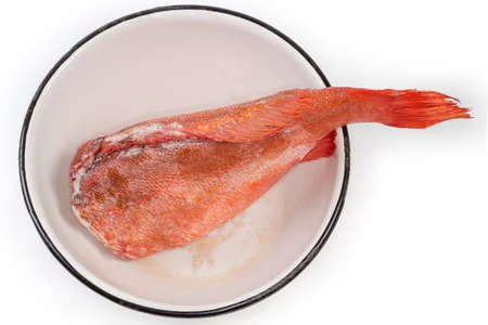 Raw frozen headless gutted carcass of a redfish also known as ocean perch in the old big enamel kitchen bowl during defrosting, top view on a white backgroundの写真素材