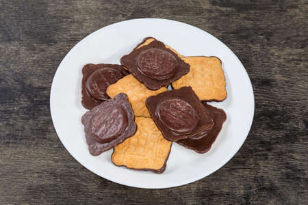Cookies square shape with chocolate coating on one side and jam filling on a white dish on a black...