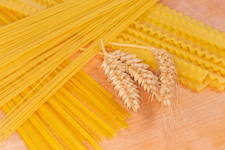 Raw long pasta of different varieties with wheat ears on a wooden board, close-up in selective focusの写真素材