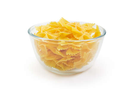 Raw bow-tie shaped pasta known as farfalle in a glass bowl, side view on a white background