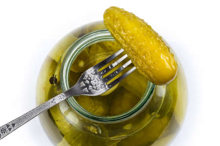 Canned cucumber on the fork atop the open big jar with the same cucumbers, top view on a white backgroundの写真素材