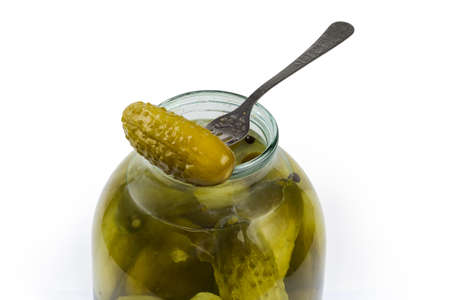 Canned cucumber on the fork atop the open big jar with the same cucumbers on a white backgroundの写真素材