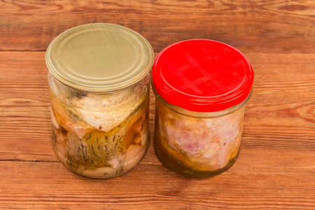 Braised pork and canned fish in its own juice in two sealed small glass jars on an old rustic table