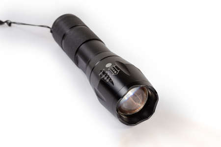 Modern tactical electric LED flashlight in black housing with zooming of the light beam on a white...