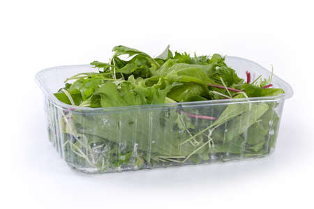 Mix of the different leaf vegetables in the transparent plastic container on a white background, side viewの写真素材