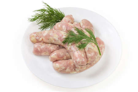 Raw thick sausages made with chicken meat in a natural casing with twigs of fresh dill on the white dish on a white backgroundの写真素材