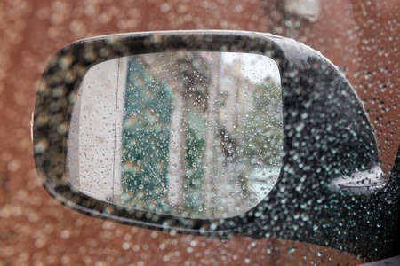 Wet car outside rear view mirror covered with water drops during a rain, inside view in selective focus through the side windowの写真素材