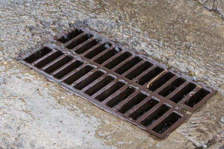Rainwater flowing down the impervious concrete surface to the storm drain equipped with cast iron...