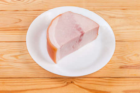 Piece of boiled smoked ham on skin on the white dish on the rustic tableの写真素材